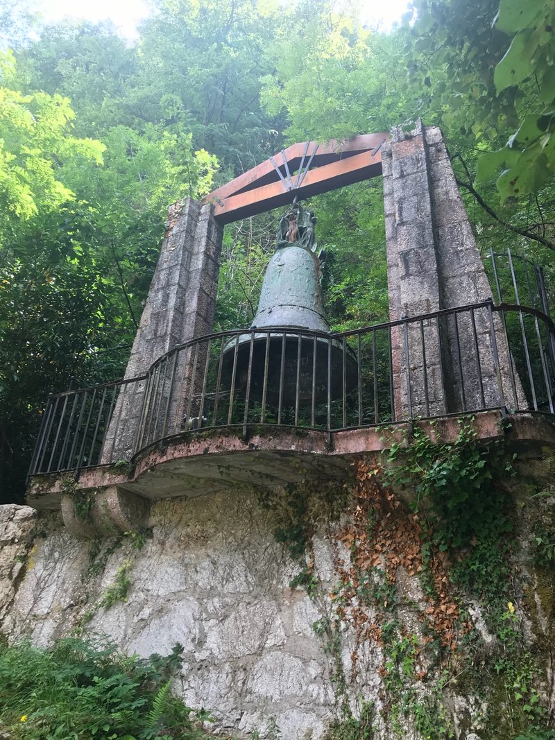 A huge bronze bell hanging in a stone frame in the forest at Covadonga